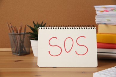 Photo of Notebook with word SOS and stationery on wooden table at workplace