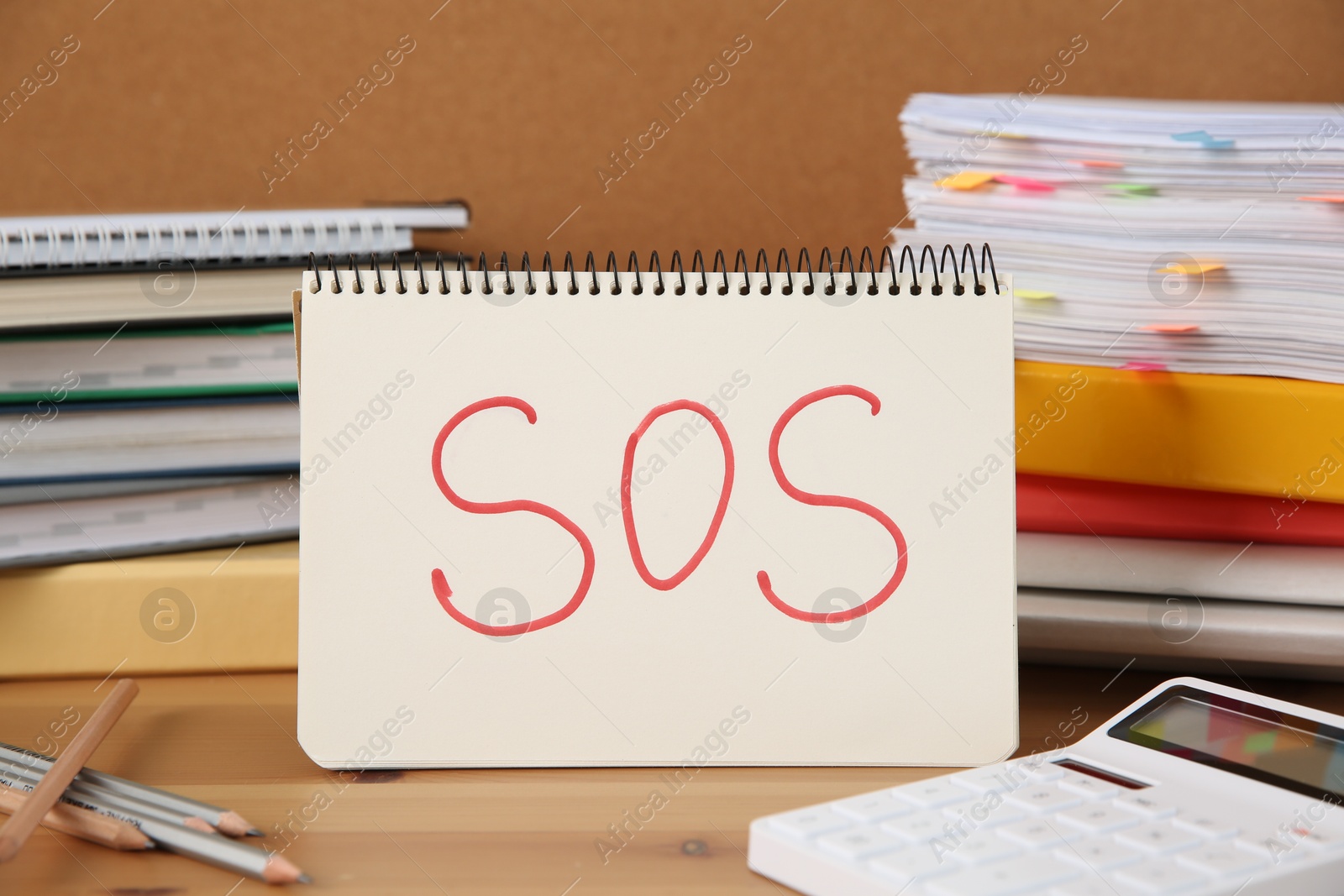 Photo of Notebook with word SOS and stationery on wooden table at workplace