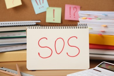 Photo of Notebook with word SOS and stationery on wooden table at workplace