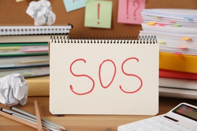 Photo of Notebook with word SOS and stationery on wooden table at workplace