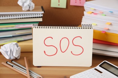 Photo of Notebook with word SOS and stationery on wooden table at workplace