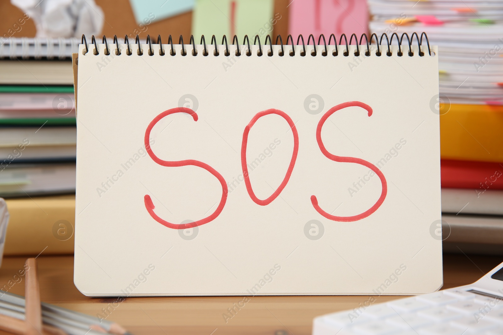 Photo of Notebook with word SOS and stationery on wooden table at workplace