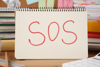 Photo of Notebook with word SOS and stationery on wooden table at workplace