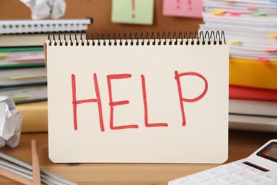 Photo of Notebook with word Help and stationery on wooden table at workplace