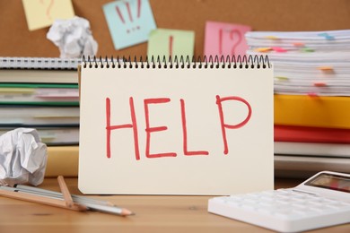 Photo of Notebook with word Help and stationery on wooden table at workplace