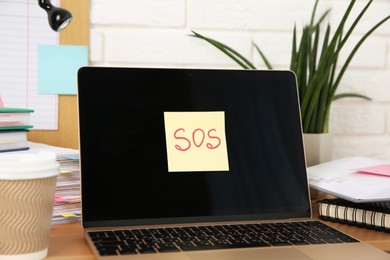 Photo of Note with word SOS, laptop and stationery on wooden table at workplace