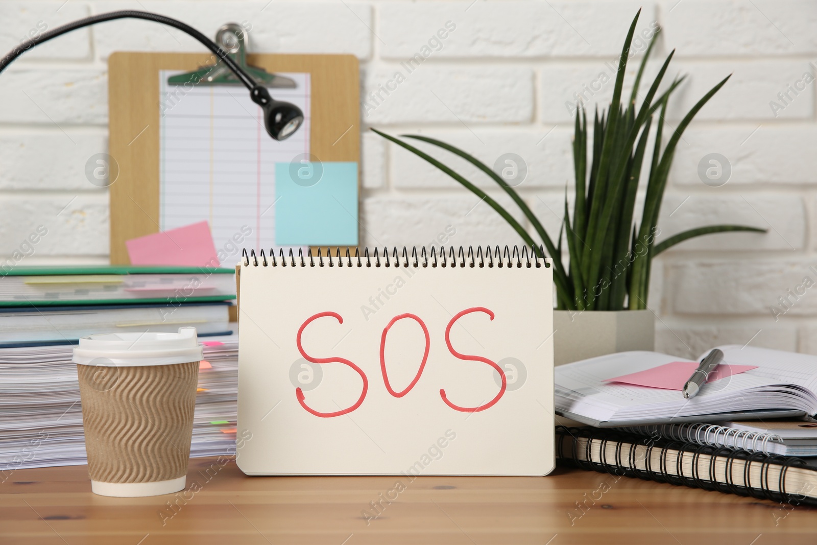 Photo of Notebook with word SOS and stationery on wooden table at workplace