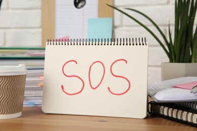 Photo of Notebook with word SOS and stationery on wooden table at workplace