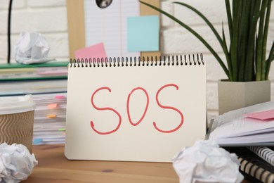 Photo of Notebook with word SOS and stationery on wooden table at workplace