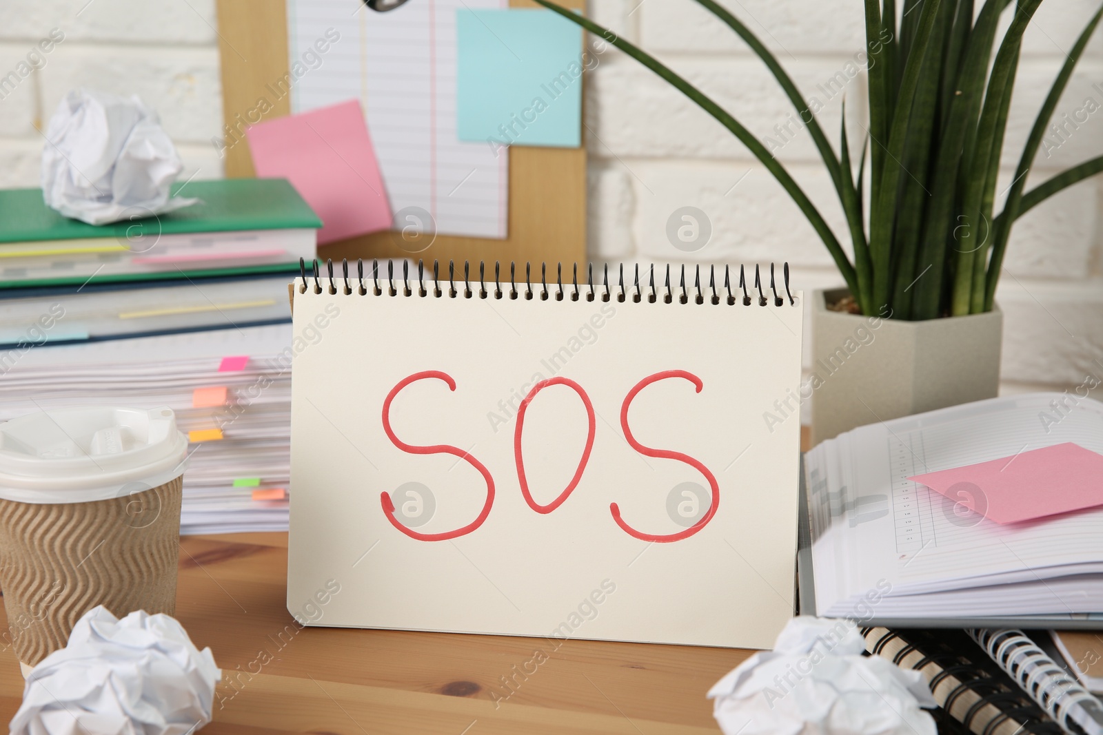 Photo of Notebook with word SOS and stationery on wooden table at workplace