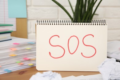 Photo of Notebook with word SOS and stationery on wooden table at workplace