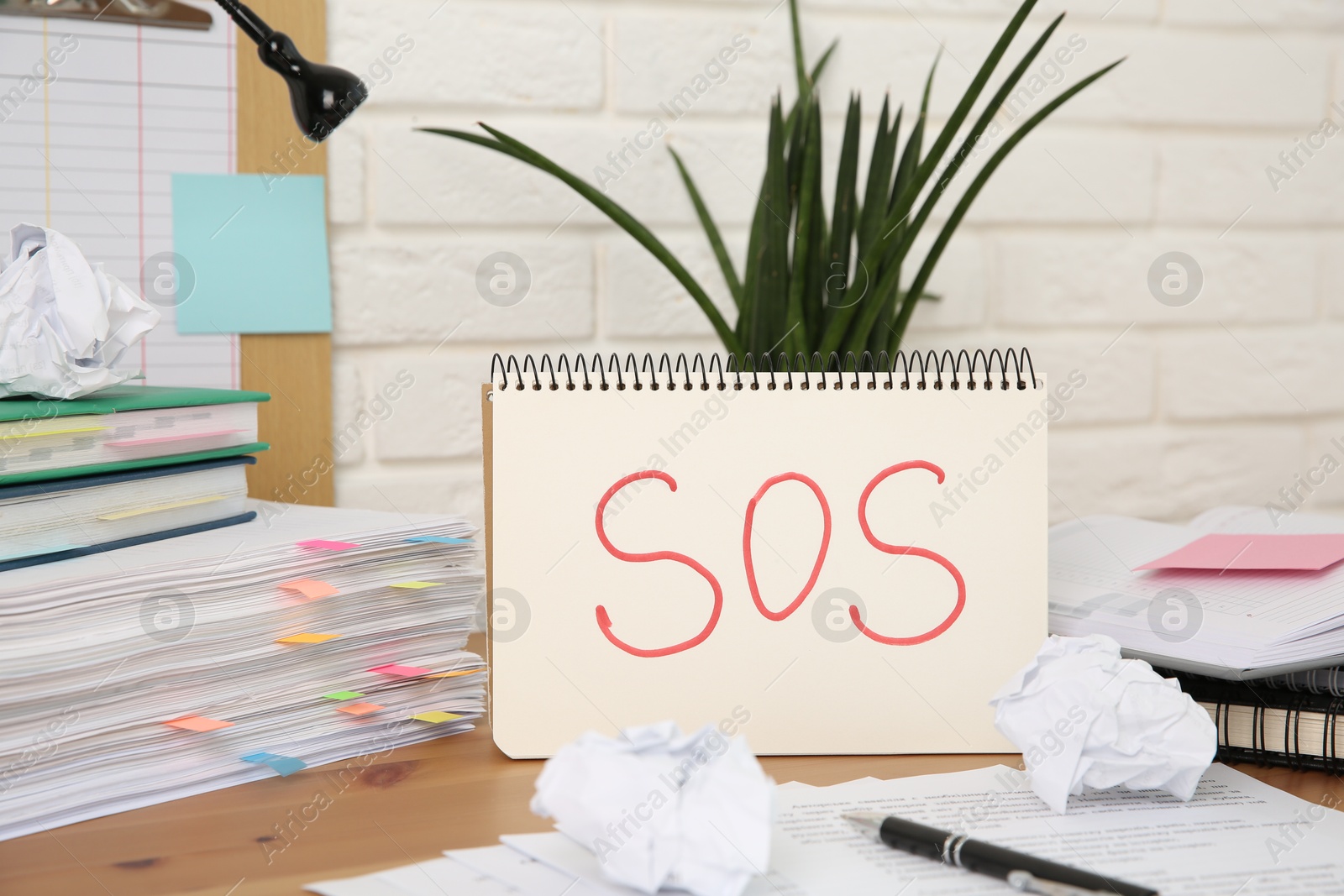 Photo of Notebook with word SOS and stationery on wooden table at workplace