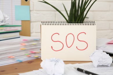 Photo of Notebook with word SOS and stationery on wooden table at workplace