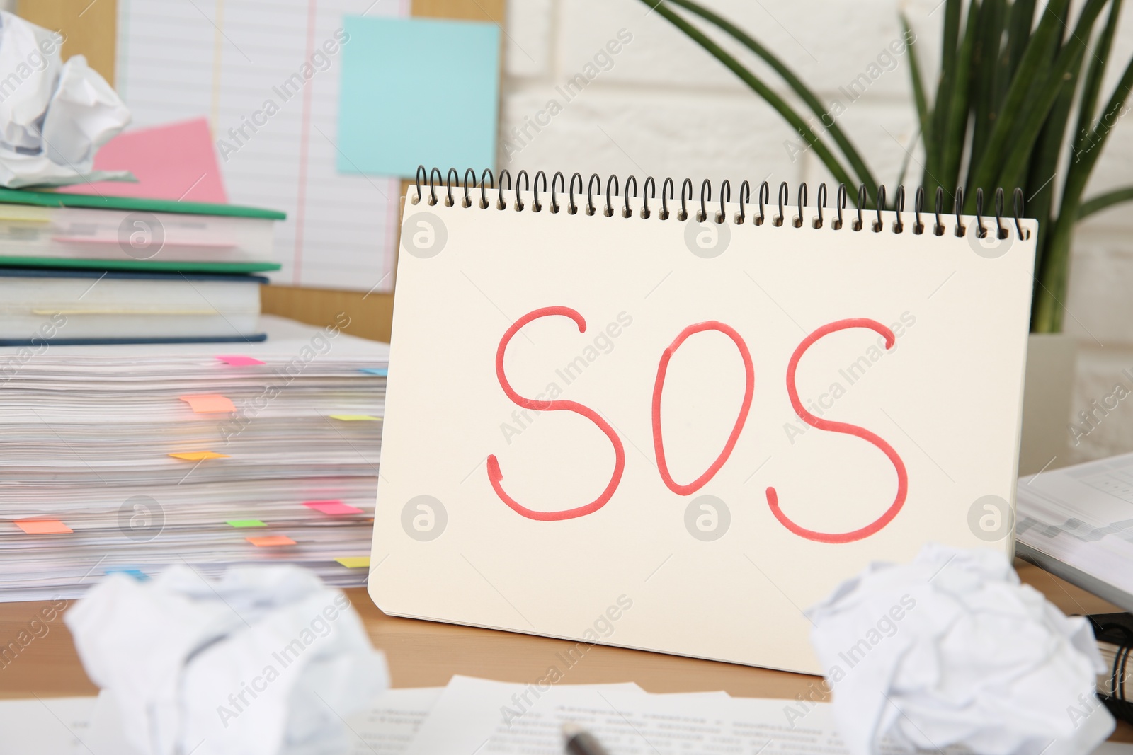 Photo of Notebook with word SOS and stationery on wooden table at workplace