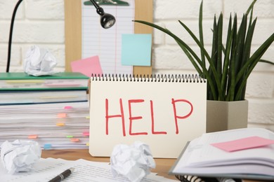 Photo of Notebook with word Help and stationery on wooden table at workplace