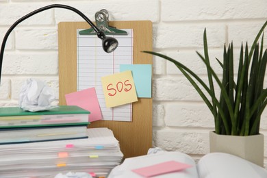 Photo of Note with word SOS and stationery on table at workplace