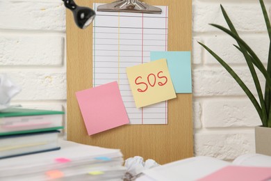 Photo of Note with word SOS and stationery on table at workplace