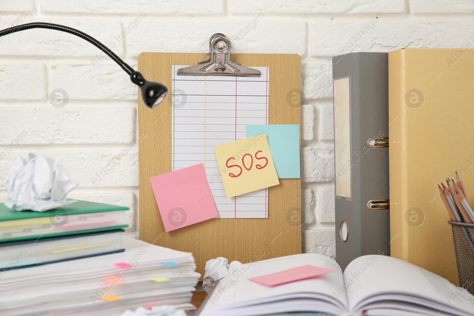 Photo of Note with word SOS and stationery on table at workplace