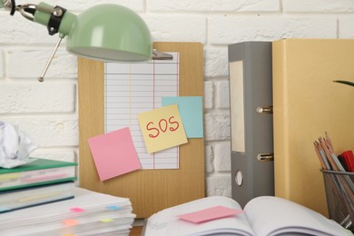 Photo of Note with word SOS and stationery on table at workplace