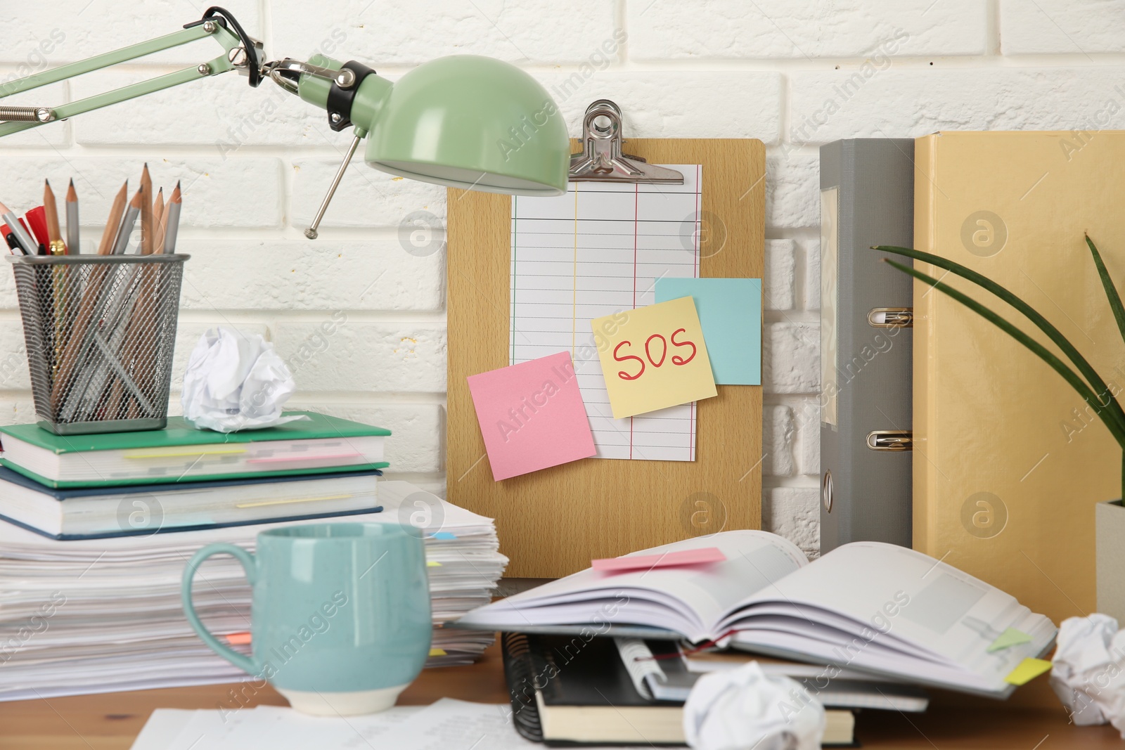 Photo of Note with word SOS and stationery on table at workplace