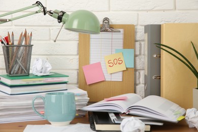 Photo of Note with word SOS and stationery on table at workplace