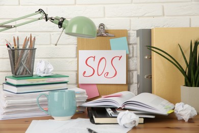 Photo of Note with word SOS and stationery on table at workplace