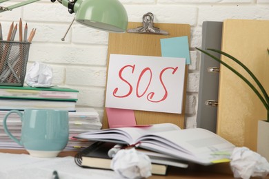 Photo of Note with word SOS and stationery on table at workplace