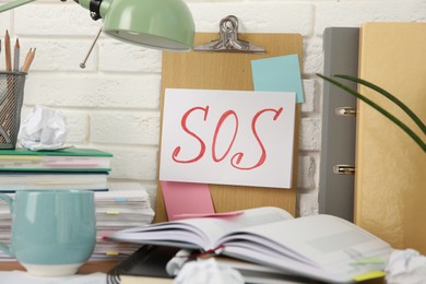 Photo of Note with word SOS and stationery on table at workplace