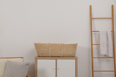 Photo of Armchair with cushion, wicker basket on nightstand and wooden ladder in room