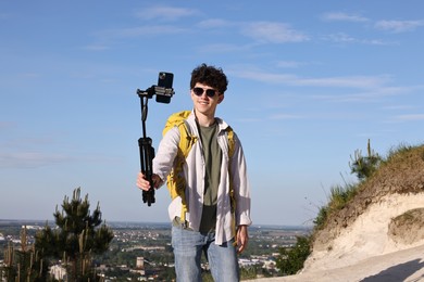 Travel blogger in sunglasses with smartphone streaming outdoors