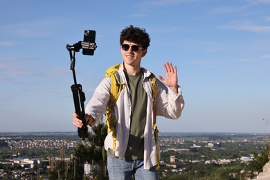 Photo of Travel blogger in sunglasses with smartphone streaming outdoors