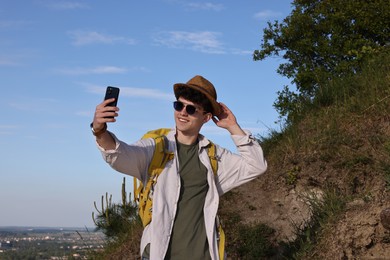 Photo of Travel blogger in sunglasses takIng selfie with smartphone outdoors