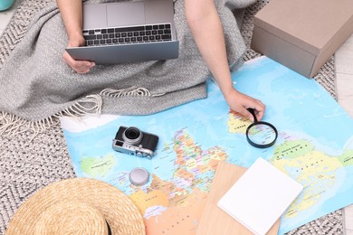 Travel blogger with magnifying glass, laptop and map planning trip at home, closeup
