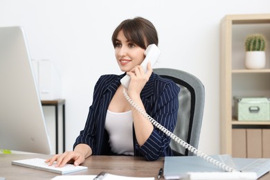 Smiling secretary talking on telephone at table in office