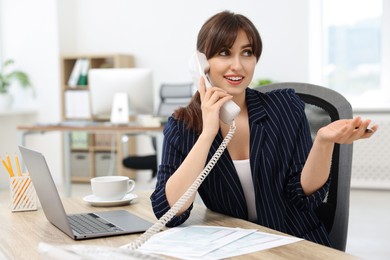 Photo of Smiling secretary talking on telephone at table in office
