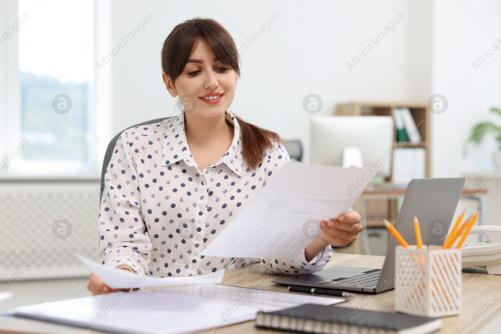 Photo of Smiling secretary doing paperwork at table in office