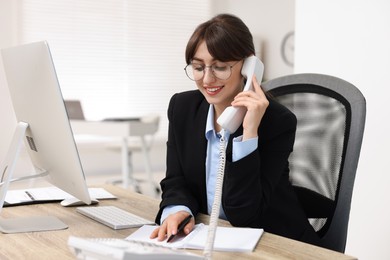Photo of Smiling secretary talking on telephone at table in office