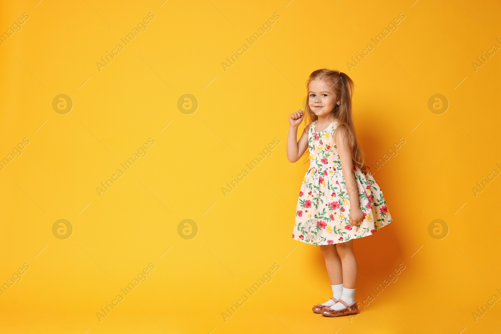 Photo of Cute little girl dancing on orange background, space for text