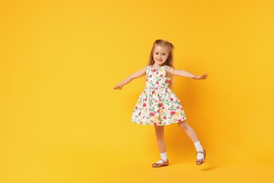 Photo of Cute little girl dancing on orange background, space for text
