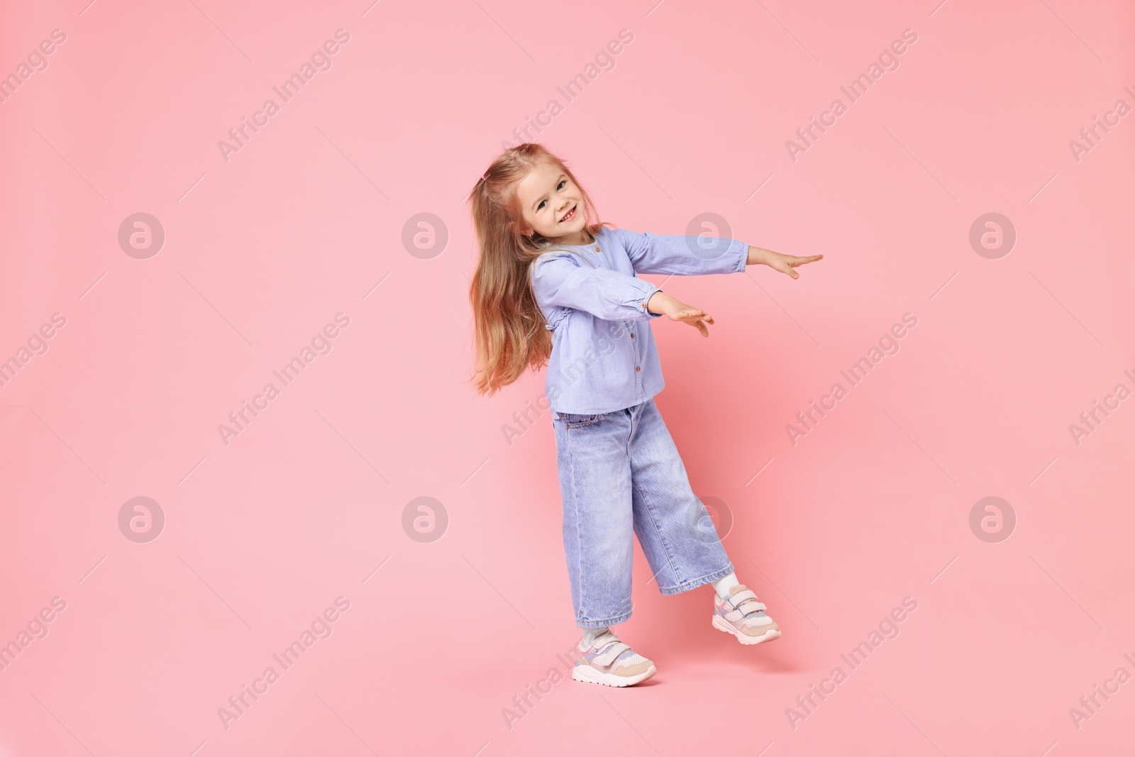 Photo of Cute little girl dancing on pink background