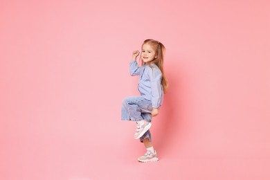 Photo of Cute little girl dancing on pink background