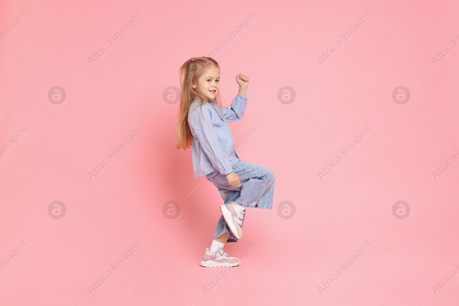 Photo of Cute little girl dancing on pink background