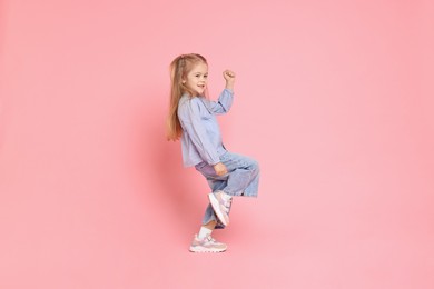 Photo of Cute little girl dancing on pink background