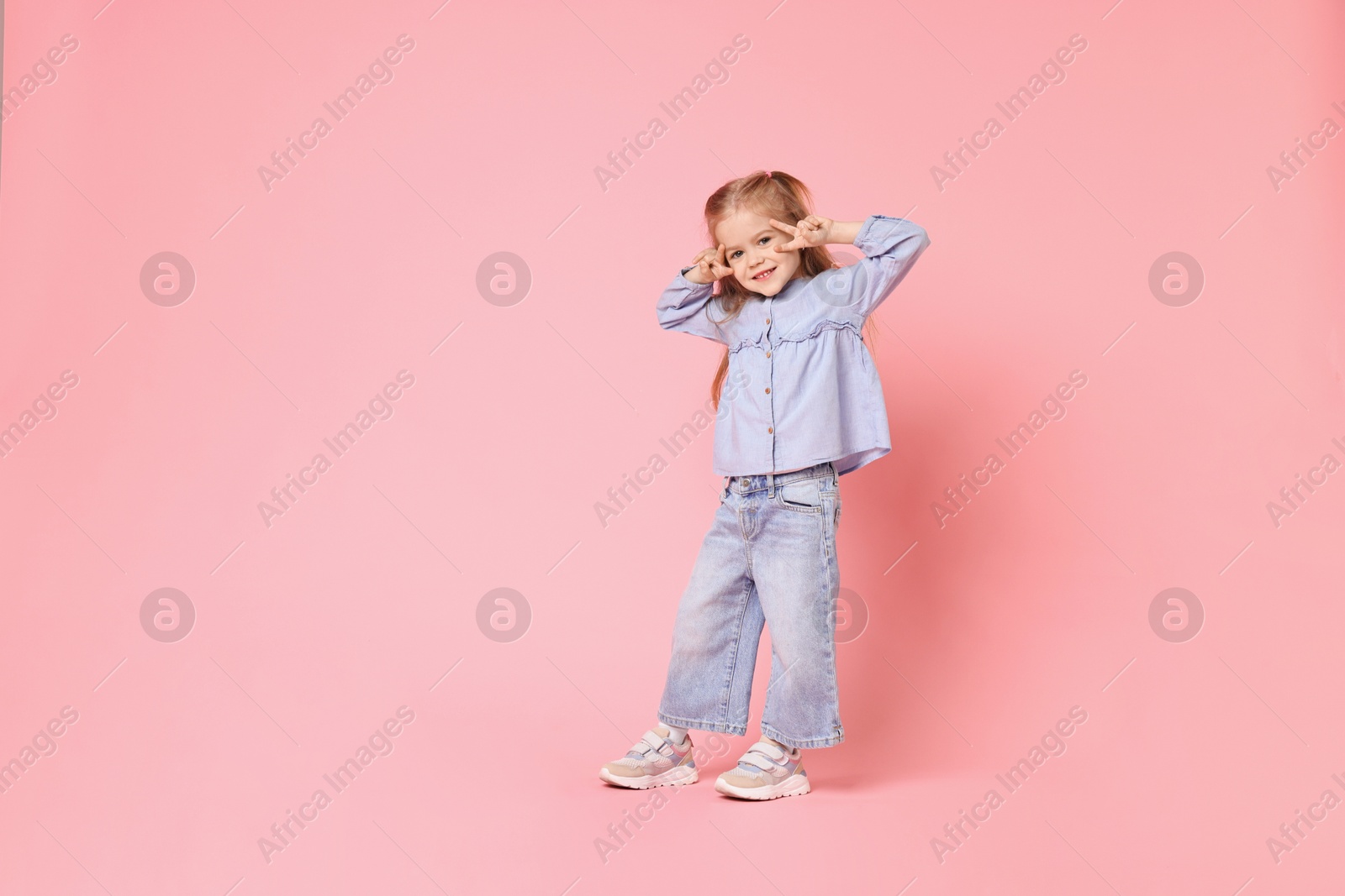 Photo of Cute little girl dancing on pink background, space for text