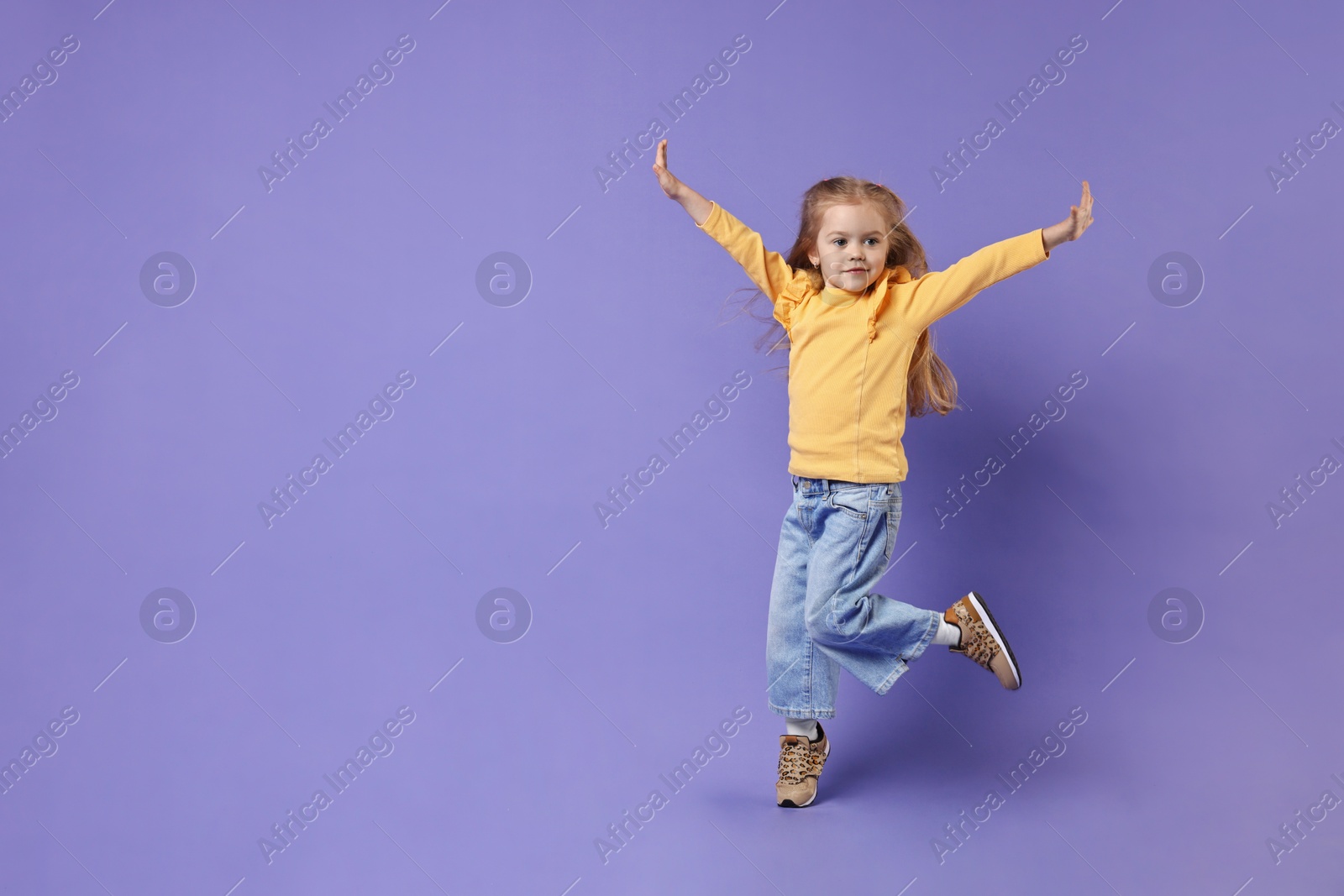 Photo of Cute little girl dancing on purple background, space for text