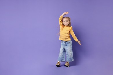 Photo of Cute little girl dancing on purple background, space for text