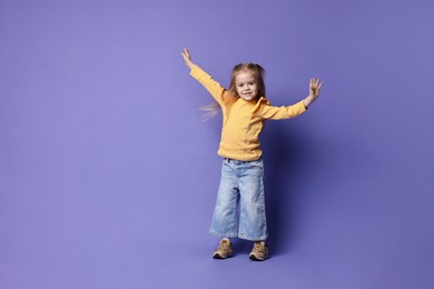 Photo of Cute little girl dancing on purple background, space for text