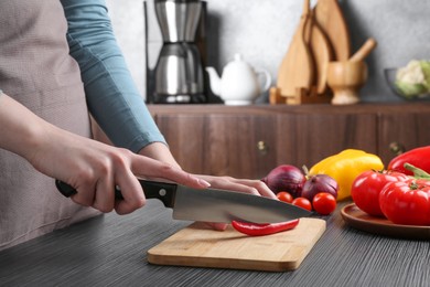 Photo of Healthy food. Woman cutting chili pepper at black wooden table, closeup