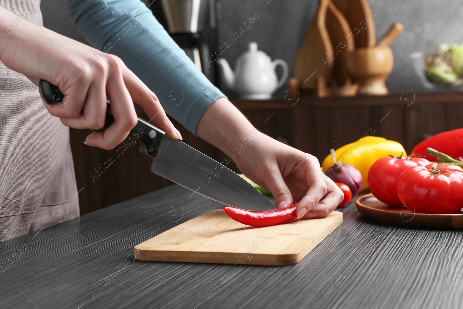 Photo of Healthy food. Woman cutting chili pepper at black wooden table, closeup