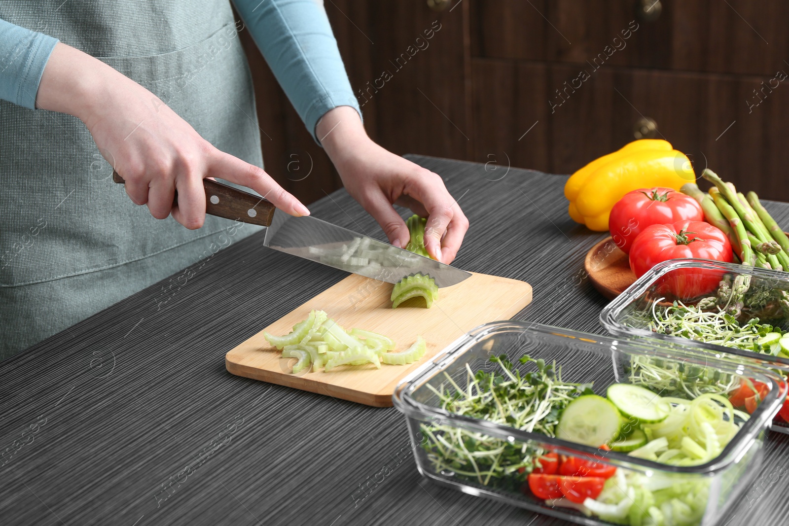 Photo of Healthy food. Woman cutting celery at black wooden table, closeup